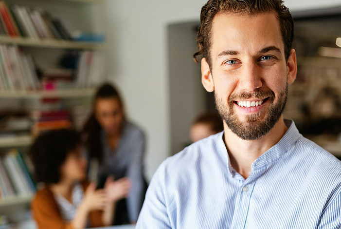 Young man smiling in a modern office with colleagues in the background