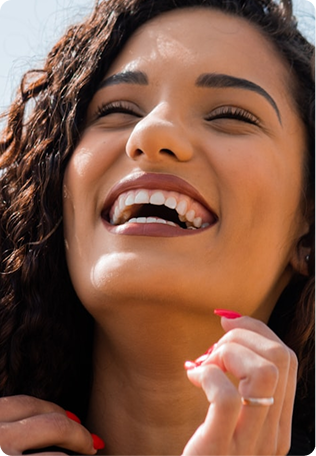 Close-up of a woman with curly hair laughing and showing a healthy, bright white smile.